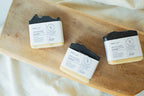 Three bars of lip balm soap from the brand Libers, labeled 'LIP Balm Soap', arranged on a wooden board over a white fabric background.