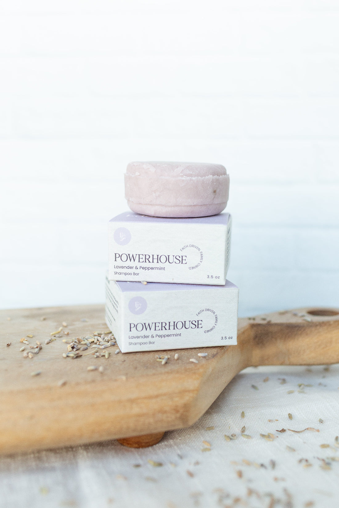 Two boxes of POWERHOUSE Lavender & Peppermint Hand Soap stacked on a wooden board, with one pale pink soap bar resting on top, against a bright white background.